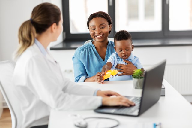 medicine, healthcare and pediatry concept - happy african american mother with baby son and caucasian doctor with laptop computer at clinic
